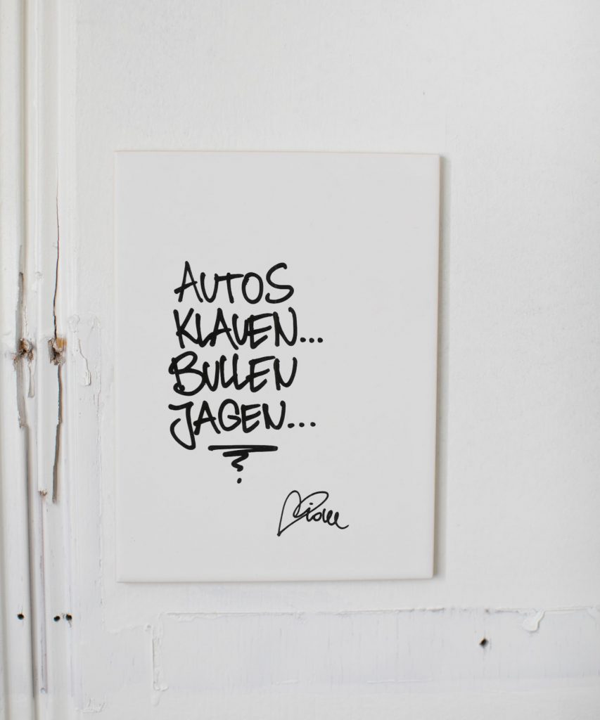 Streetartis idee schreibt "Autos klauen, bullen jagen". Weiße Wandkachel für deine Wand zuhause. Foto von Nina Bröll.